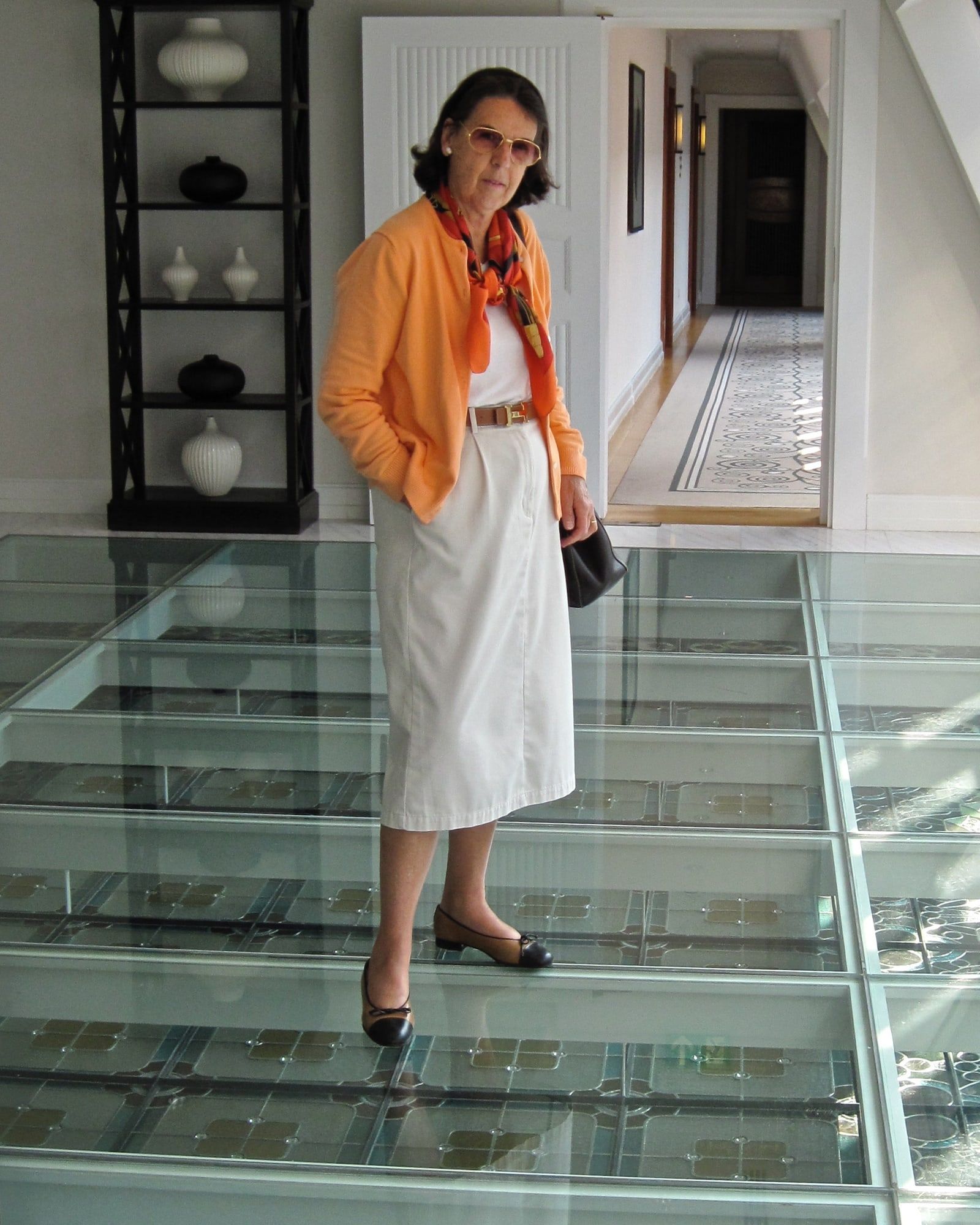 Eveline Henner in an orange cardigan and silk scarf, standing on a glass floor above a stained-glass ceiling.